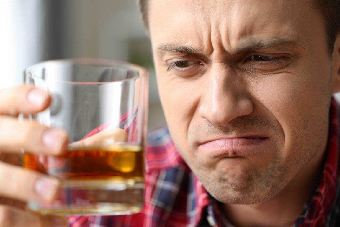 Мужчина держит бокал и кривится на него